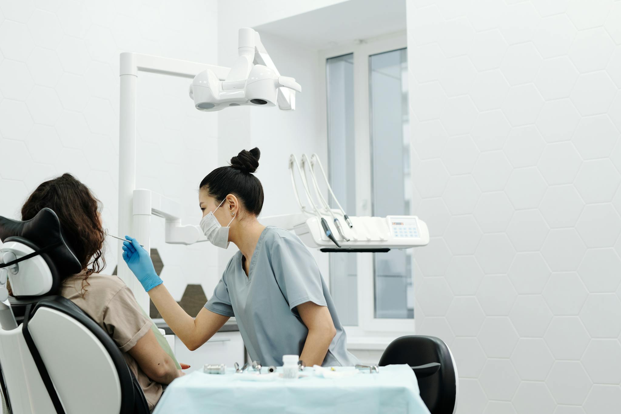 A dentist wearing protective gear examines a patient in a modern clinic setting.