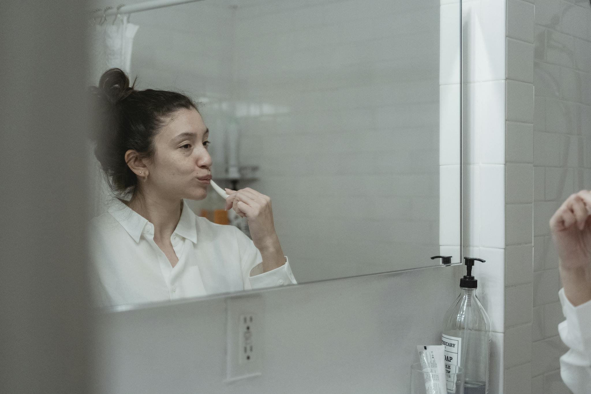 Adult woman brushing teeth, reflected in bathroom mirror. Clean and minimal style.
