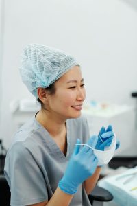 Asian female doctor in scrubs and PPE smiling during a break in a medical clinic.