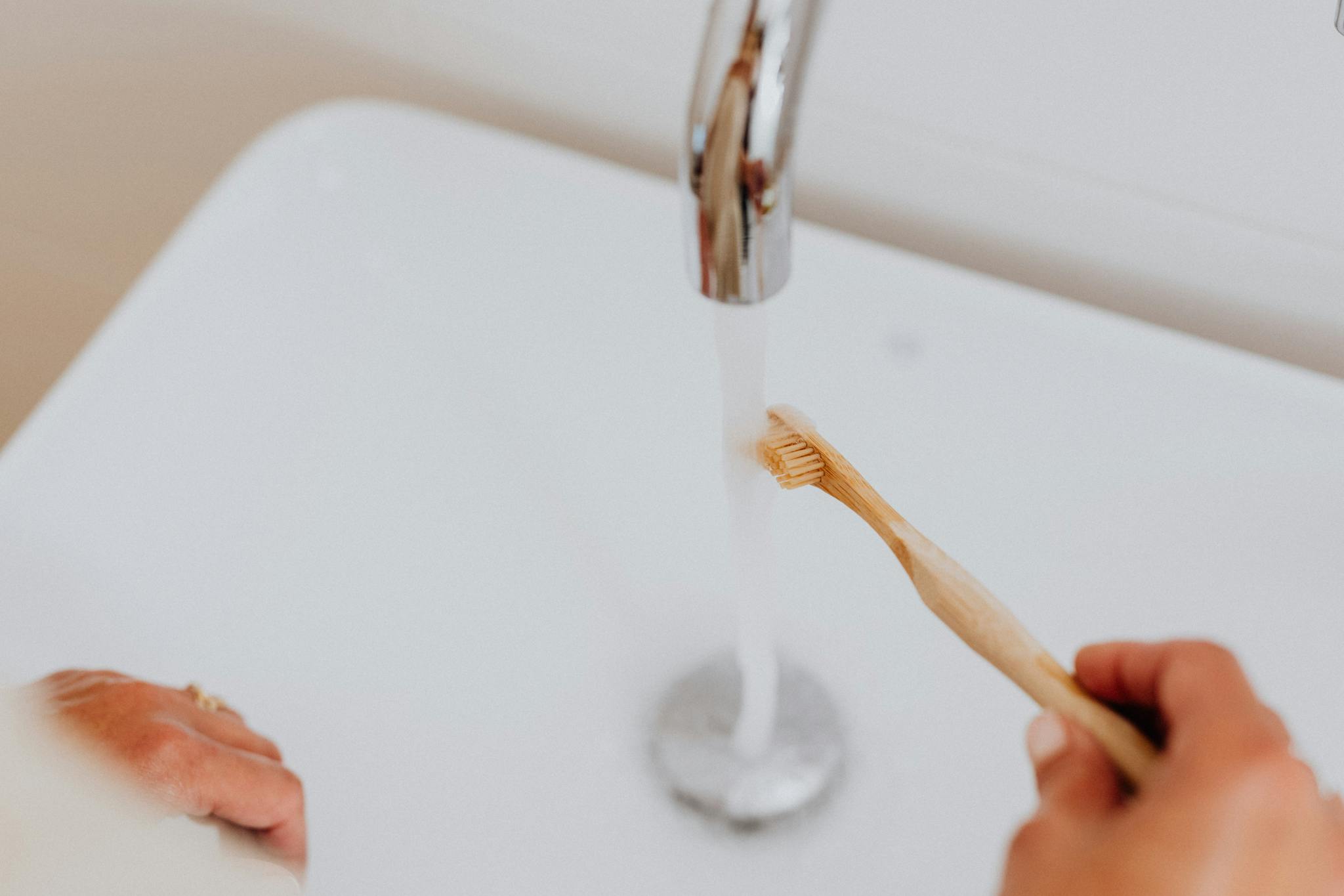 Close-up of a bamboo toothbrush under a running faucet, promoting sustainable living.